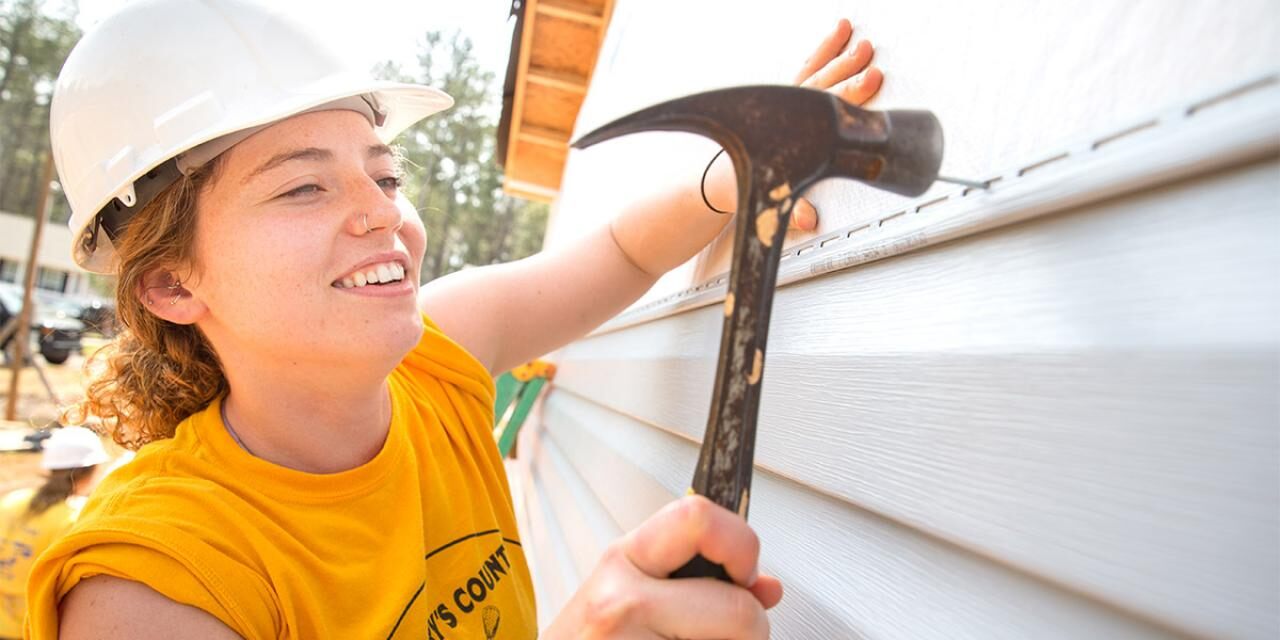 Collegiate Challenge volunteer using a hammer on a Habitat build